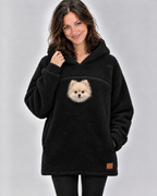 Woman in a black pouch hoodie with a small cream Pomeranian peeking out of the chest opening