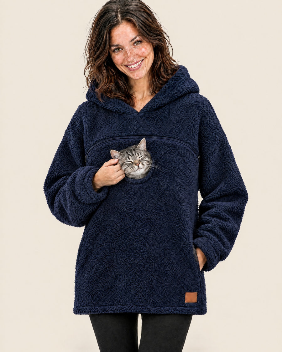 Woman in a navy tucked pouch hoodie cupping the cheek of the silver tabby cat peeking out of the chest opening